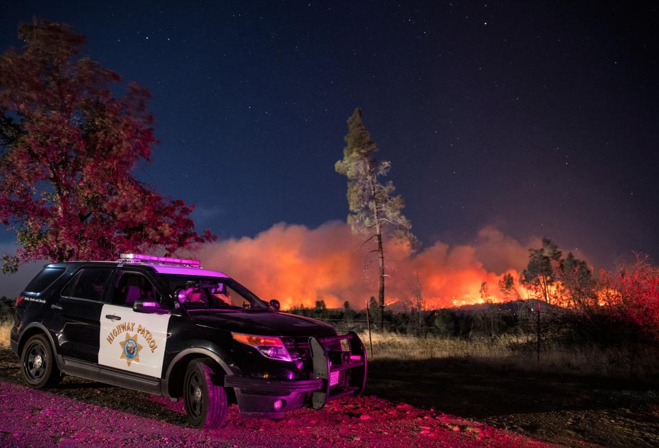 In this Sept. 28, 2020, file photo, a California Highway Patrol officer watches flames visible from the Zogg Fire near Igo, Calif. Pacific Gas & Electric will face criminal charges because its equipment sparked the wildfire that killed four people and destroyed hundreds of homes, Shasta County District Attorney Stephanie Bridgett announced Thursday, July 29, 2021.