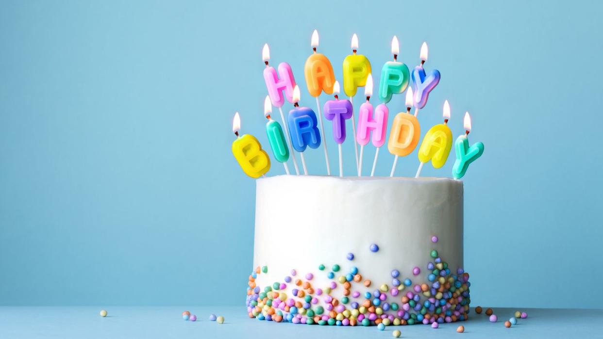 colorful birthday cake with candles spelling happy birthday set against a blue background