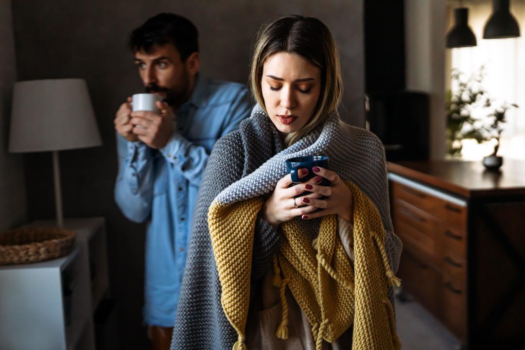 Freezing couple covered with a blanket. Man and a woman wrapped in a warm blanket in a cold room.