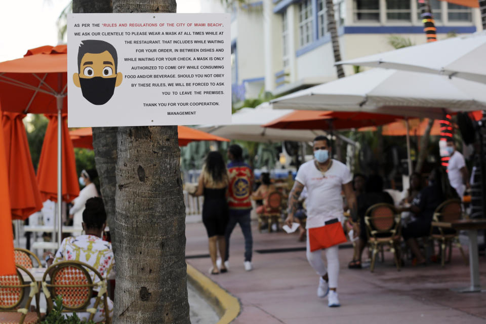 FILE - In this July 24, 2020, file photo, a sign informs customers at the Edison Hotel restaurant about wearing a protective face mask during the coronavirus pandemic, along Ocean Drive in Miami Beach, Fla. Families trying to get in a last-minute vacation before school starts better do some homework on COVID-19 restrictions before loading up the minivan. (AP Photo/Lynne Sladky, File)