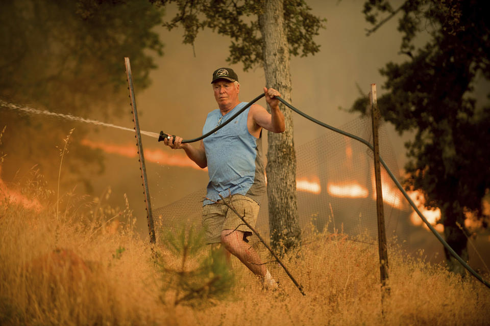 <p>Jim Berglund sprays water while defending his home as a wildfire approaches on Saturday, July 8, 2017, near Oroville, Calif. Although flames leveled Berglund’s barn, his home remained unscathed as the main fire head passed. (AP Photo/Noah Berger) </p>