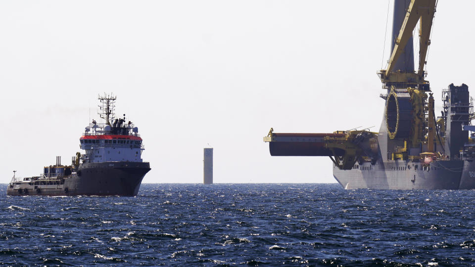 A monopile hangs over the deck of the crane ship Bokalift 2, flagged in Cyprus, right. Alongside is the vessel Bear, flagged in Belgium, at the South Fork Wind project, Tuesday, July 11, 2023, off the coast of Rhode Island. The trade association that represents the offshore service industry is going to great lengths to make sure that jobs go to Americans as the U.S. offshore wind industry ramps up. At center background is a recently installed monopile, awaiting tower, turbine and blade sections. (AP Photo/Charles Krupa)