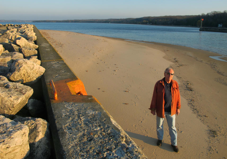 In this Nov. 16, 2012 photo, Jim Simons, who runs a rod and reel repair business in Onekama, Mich., strolls on a sand bar alongside the Portage Lake channel that leads to Lake Michigan at Onekama, Mich. The sand bar normally would be submerged in water, but low Great Lakes levels have exposed the shoreline in many areas, causing problems for boaters and tourist businesses in small harbor towns. The Great Lakes, the world’s biggest freshwater system, are dropping because of drought and climbing temperatures, a trend that accelerated with this year’s almost snowless winter and scorching summer. (AP Photo/John Flesher)