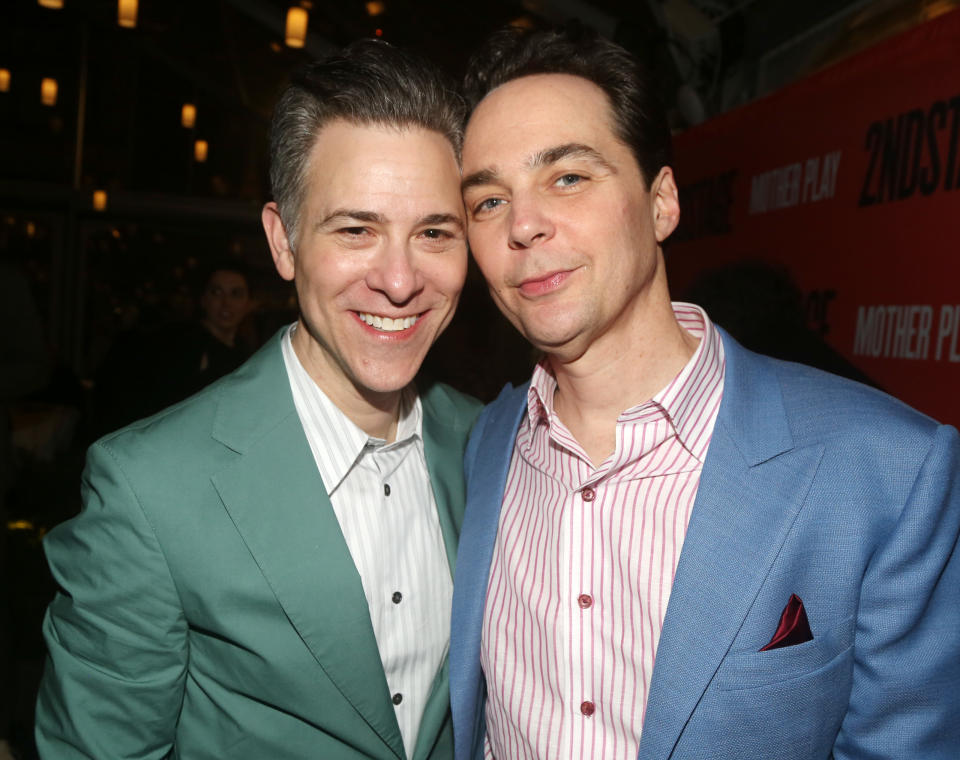 Jim Parsons and Todd Spiewak smiling and posing together, both wearing blazers, at an event with a banner in the background