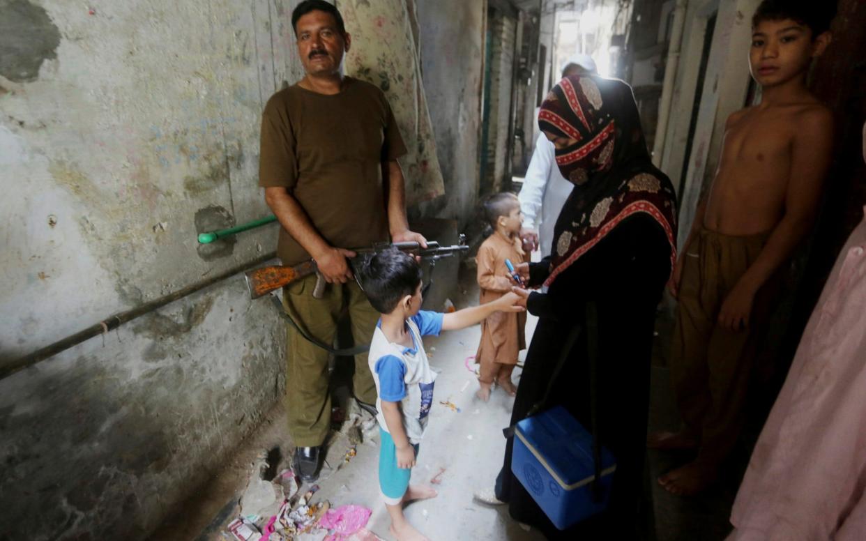 A police officer stands guard while a health worker vaccinates a child - AP