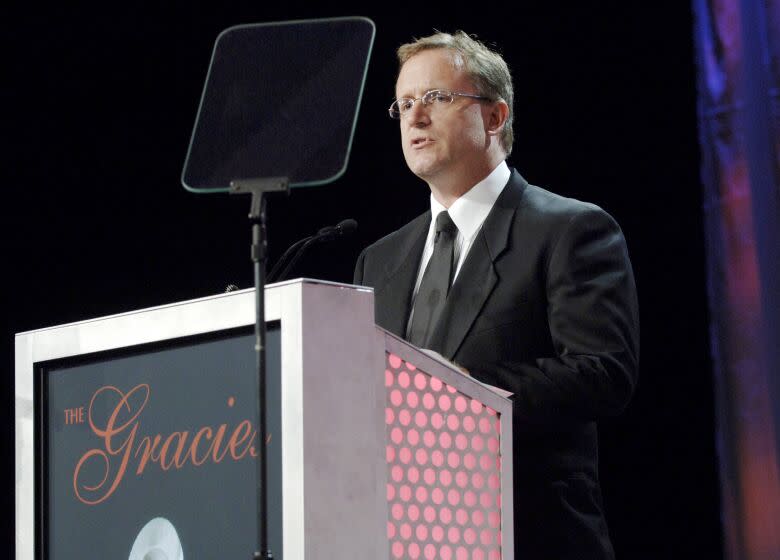 A man wearing a suit and glasses stands behind a podium that says The Gracie