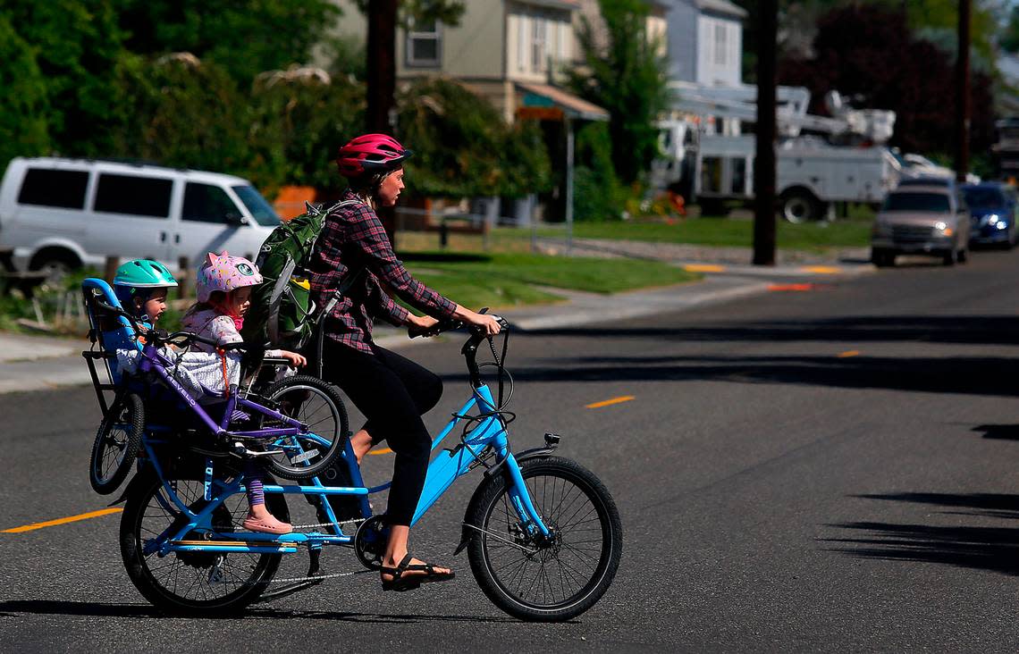 A woman with two children on a well-outfitted electric bicycle crosses Thayer Drive near Symon Street recently in Richland.