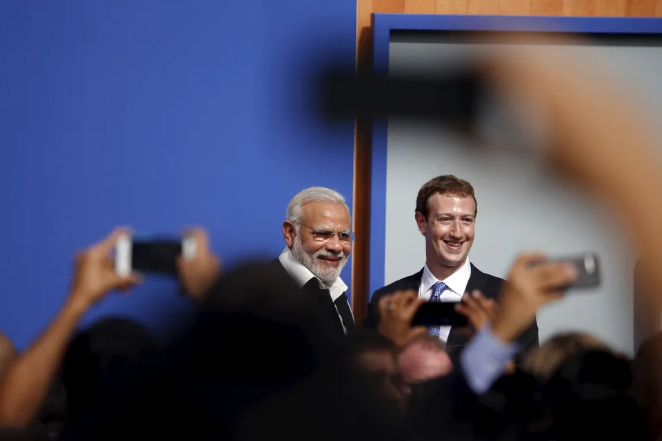 Dos hombres sonriendo de pie en un escenario. Los brazos levantados que sostienen teléfonos se pueden ver en primer plano. (Fuente: Reuters)