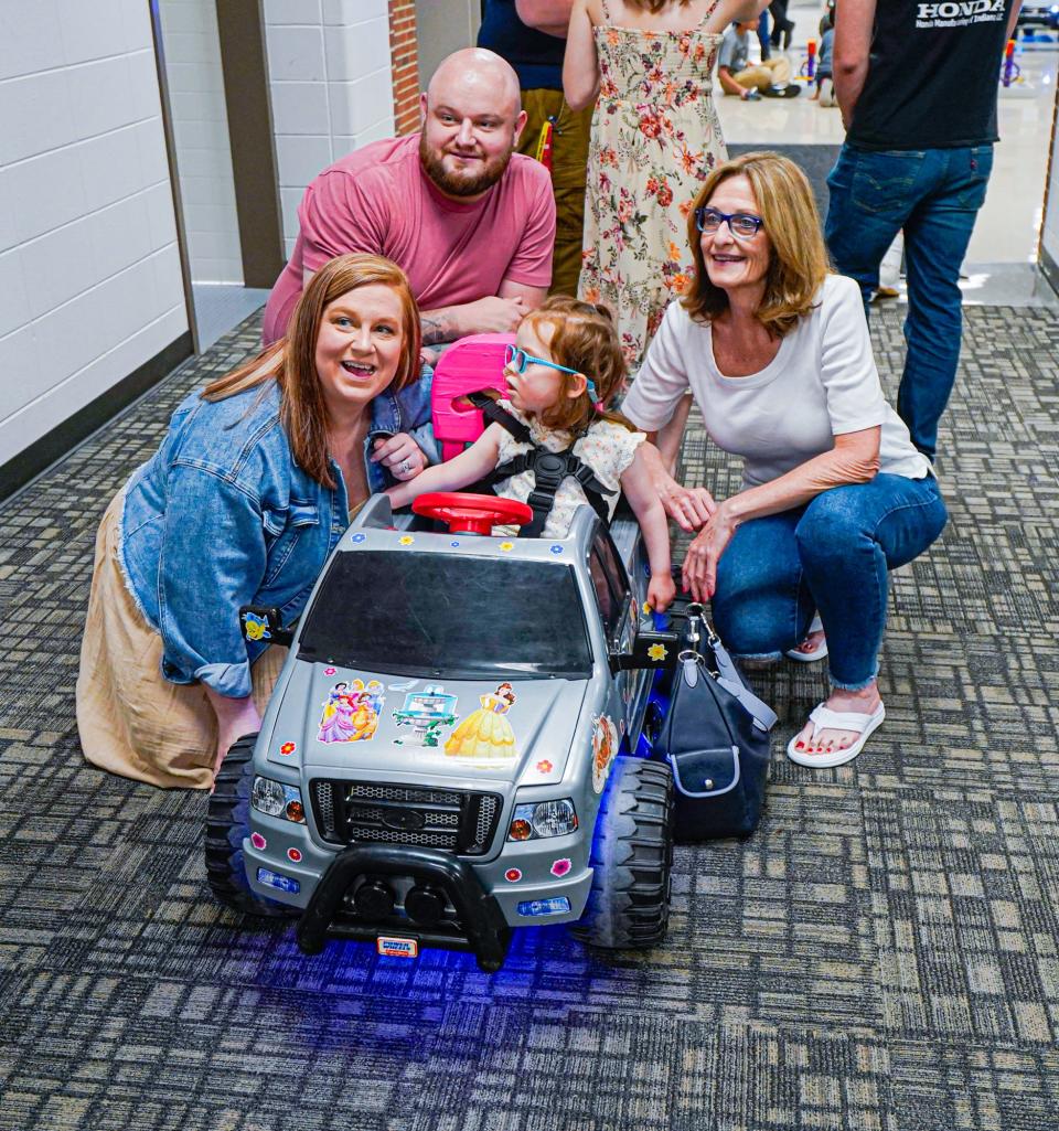 Brynlee Aydelotte, her parents Nate and Ashley Aydelotte, and grandmother Penny Smith pose for family photos with Brynlee's new ride-on electric car, custom modified by the "Mini-Movers" club and presented to children with mobility needs, during a "Night of Engineering" on Wednesday, May 10, 2023, at Southport High School in Indianapolis. 
