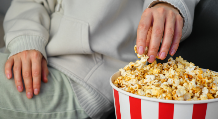 A hand dipping into a bowl of popcorn, representing entertainment industry; eating while enjoying entertainment. Entertainment stocks.