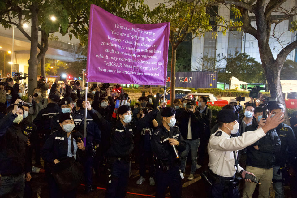 Police raise a warning flag against supporters outside a court in Hong Kong Thursday, March 4, 2021. A marathon court hearing for 47 pro-democracy activists in Hong Kong charged with conspiracy to commit subversion enters its fourth day on Thursday, as the court deliberates over whether the defendants will be granted bail. (AP Photo/Vincent Yu)