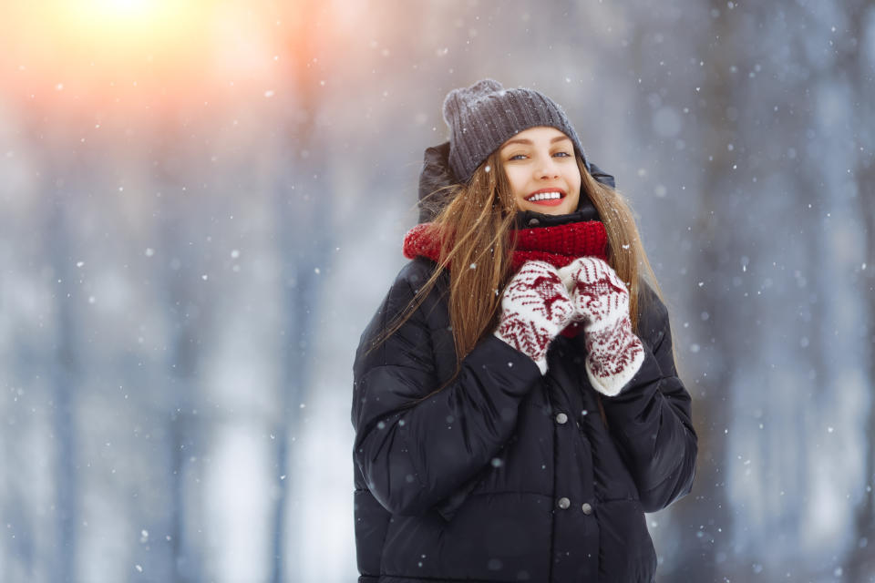 Person in winter attire smiling with hands near face, standing in snow
