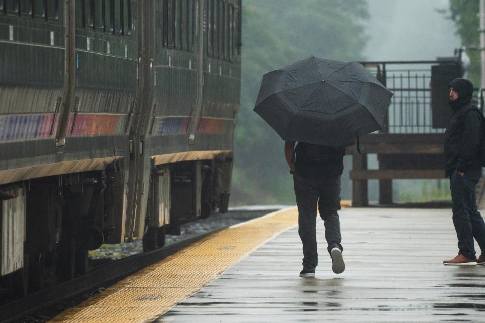 A man uses an umbrella to shield himself from the rain as he boards a northbound NJ Transit train on the Spring Valley Line in Westwood, NJ on Monday Aug. 7, 2023. 