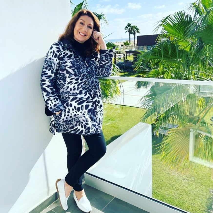 Jane McDonald standing on jotel balcony in snow leopard-print coat