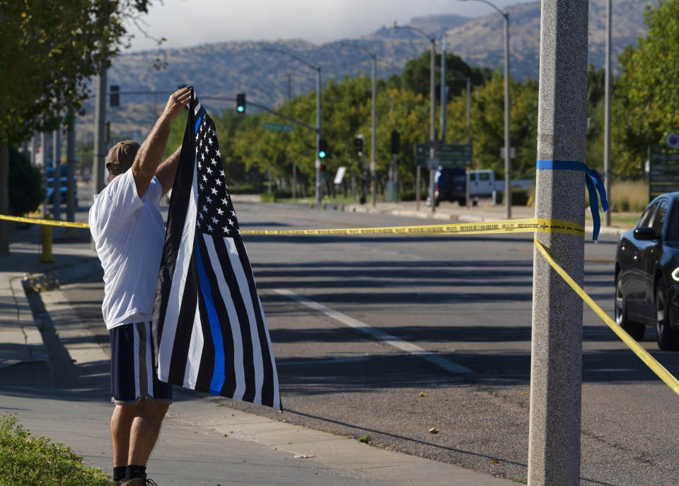 A local resident waves a Thin Blue Line flag in support of a deputy who was shot while in his patrol car in Palmdale, Calif. on Sunday, Sept. 17, 2023. A sheriff's department deputy has died after he was shot in his patrol car by an unknown assailant on Saturday, and an investigation is underway. (AP Photo/Richard Vogel)