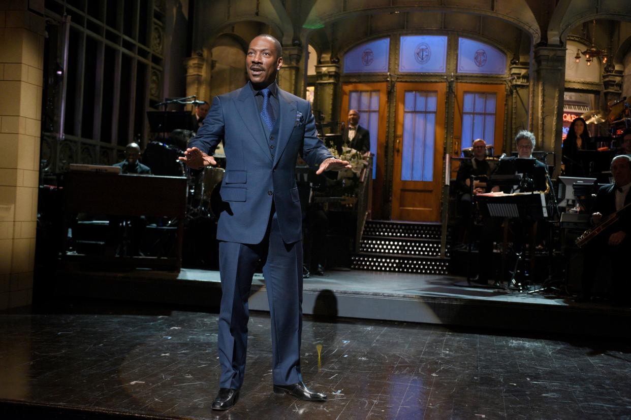 Eddie Murphy stands with his arms out palms facing down on the 'SNL' stage