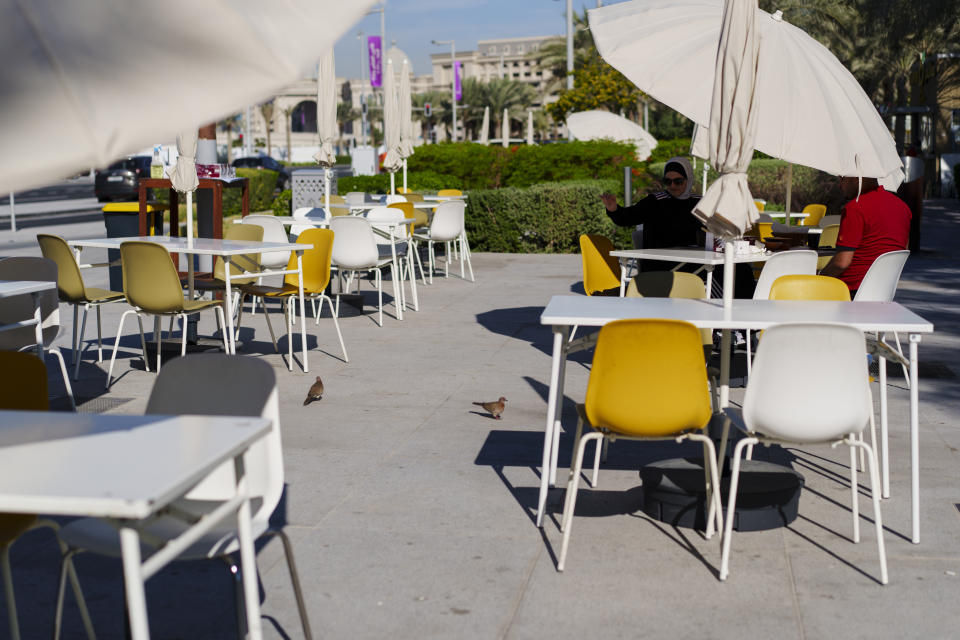 A woman feeds birds in a street cafe at Lusail Marina Corniche in Lusail downtown, Qatar, Thursday, Nov. 24, 2022. (AP Photo/Pavel Golovkin)