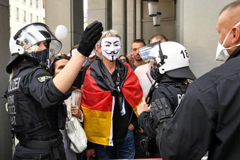 Die Polizei spricht mit einem Teilnehmer, der eine Guy Fawkes Maske trägt und eine deutsche Fahne über den Schultern hat, bei einer Demonstration gegen die Corona-Maßnahmen.<span class="copyright">Bernd von Jutrczenka / dpa</span>