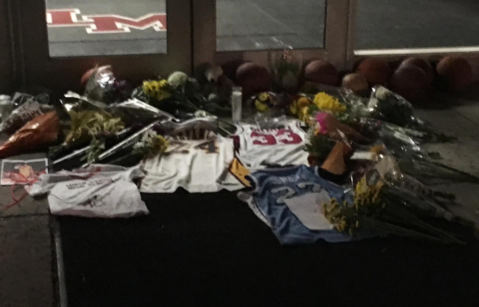 Several dozen people stand silently at Lower Merion High School, where NBN basketball star Kobe Bryant attended, in Ardmore near Philadelphia, Sunday night, Jan. 26, 2020, following reports of Bryant's death in a helicopter crash in southern California. Some embrace each other in front of Kobe Bryant Gymnasium, where flowers, basketballs, sweat shirts and candles had been laid. (AP Photo/Ron Todt)