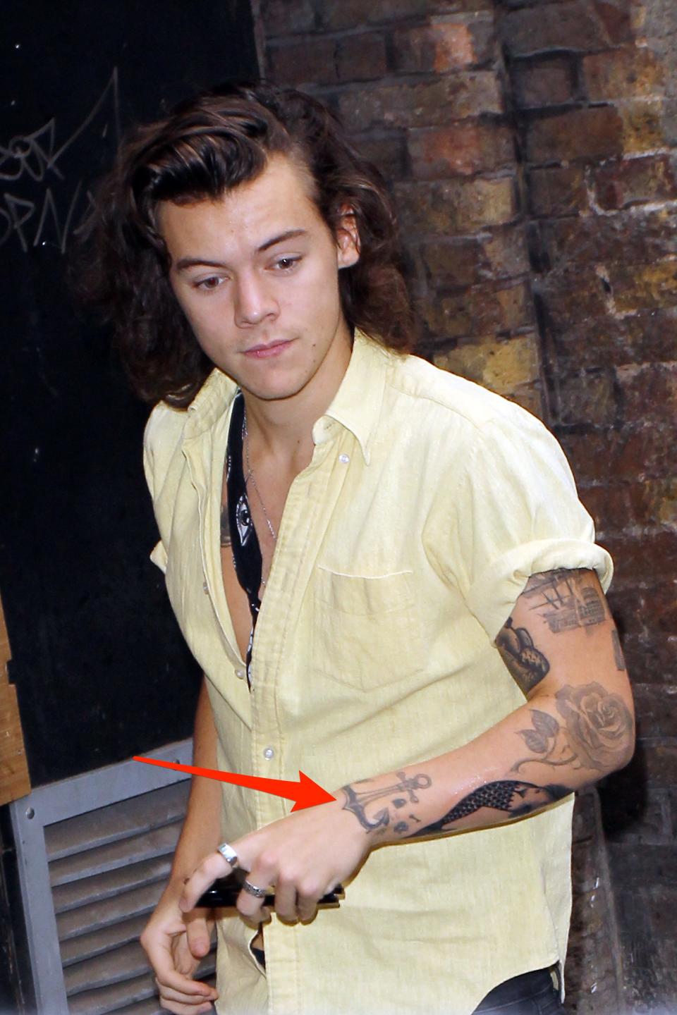 A red arrow pointing to an anchor tattoo on Harry Styles' left wrist.