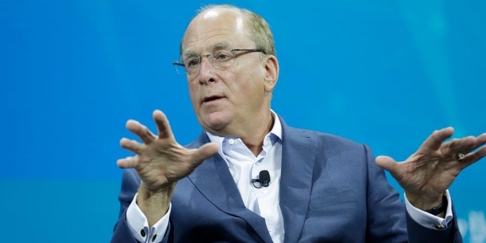 BlackRock CEO Larry Fink gestures while sitting in front of a blue screen.