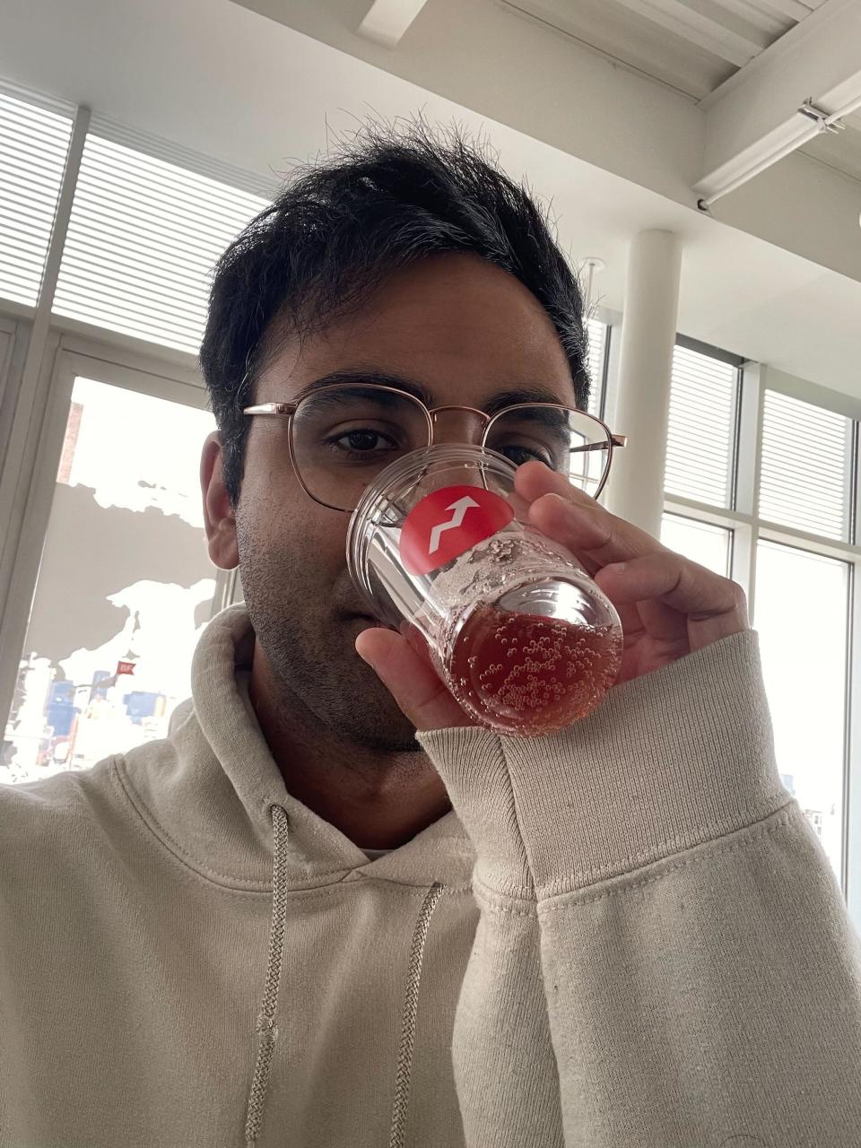 A man wearing a hoodie and drinking a beverage