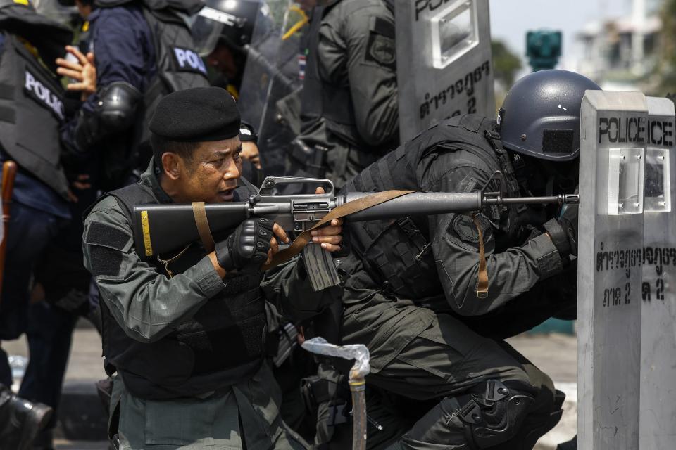 A Thai police officer aim his weapon towards anti-government protesters during clashes near Government House in Bangkok