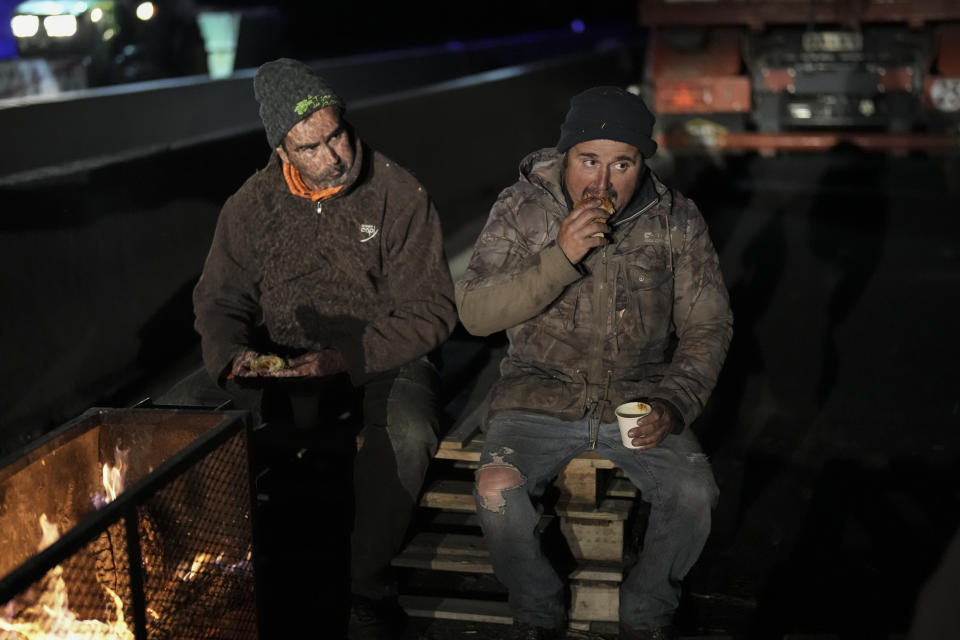 Farmers eat croissants for breakfast after spending the night at a highway barricade in Aix-en-Provence, southern France, Tuesday, Jan. 30, 2024. France's protesting farmers encircle Paris with tractor barricades, vowing a 'siege' over grievances. (AP Photo/Daniel Cole)