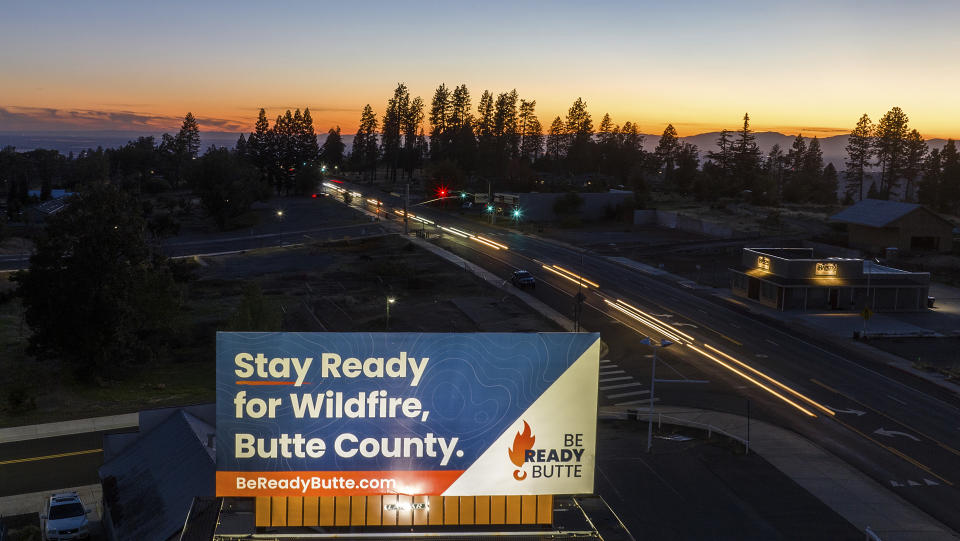 Cars pass a wildfire awareness billboard as the sun sets behind Paradise, Calif., Thursday, Oct. 26, 2023. (AP Photo/Noah Berger)