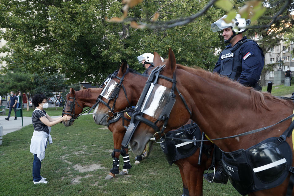 A woman touches a police horse during a demonstration in Belgrade, Serbia, Wednesday, July 8, 2020. Serbia's president Aleksandar Vucic backtracked Wednesday on his plans to reinstate a coronavirus lockdown in Belgrade after thousands protested the move and violently clashed with the police in the capital. (AP Photo/Darko Vojinovic)