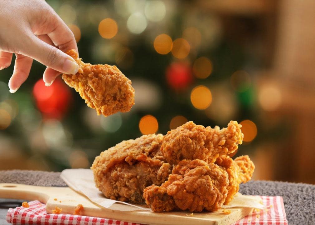 A hand picking up a fried chicken leg off a plate of more fried chicken.