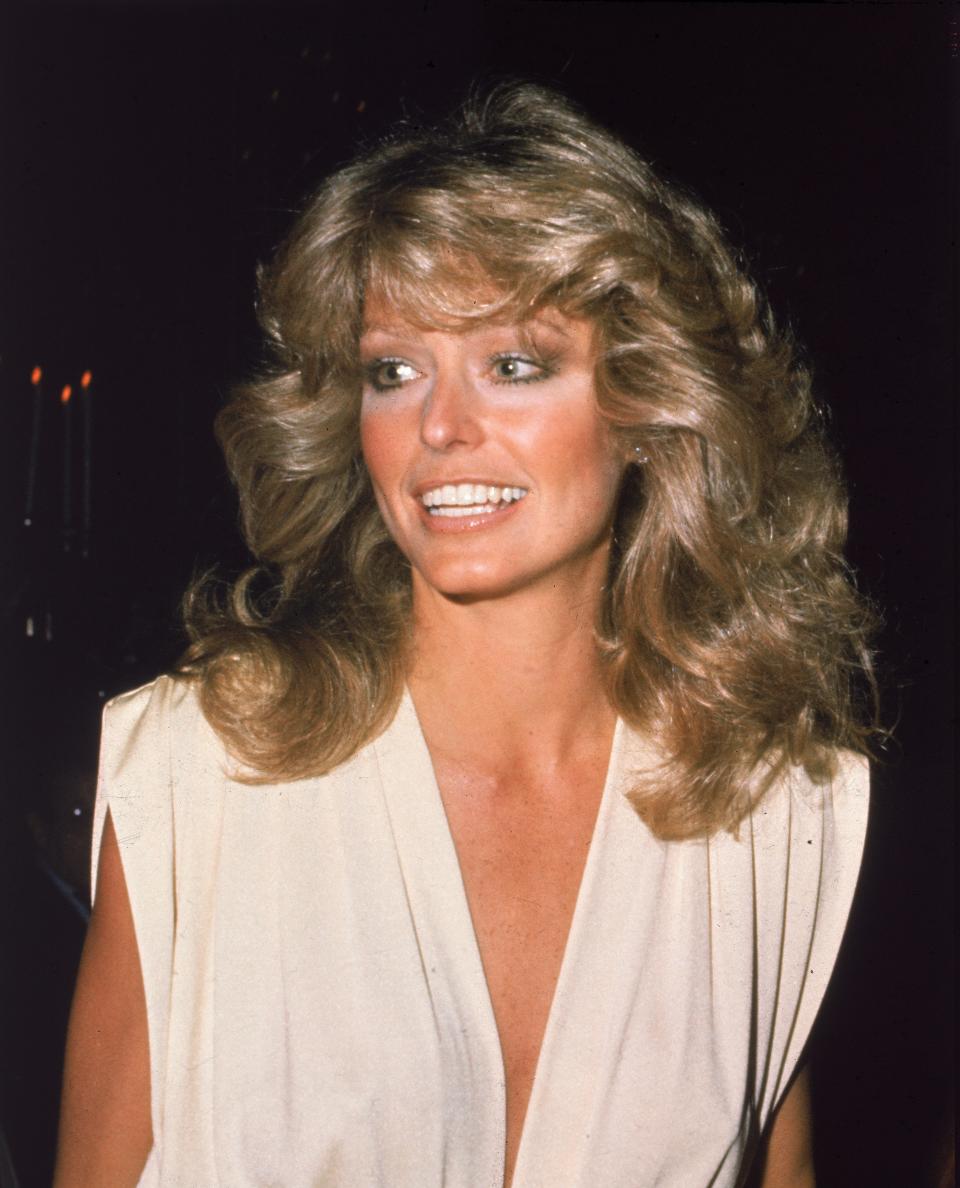 Farrah Fawcett smiling, wearing a v-neck sleeveless top, with voluminous, wavy hair