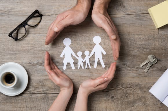 Two sets of hands on a table encircling a paper cut-out of a family.