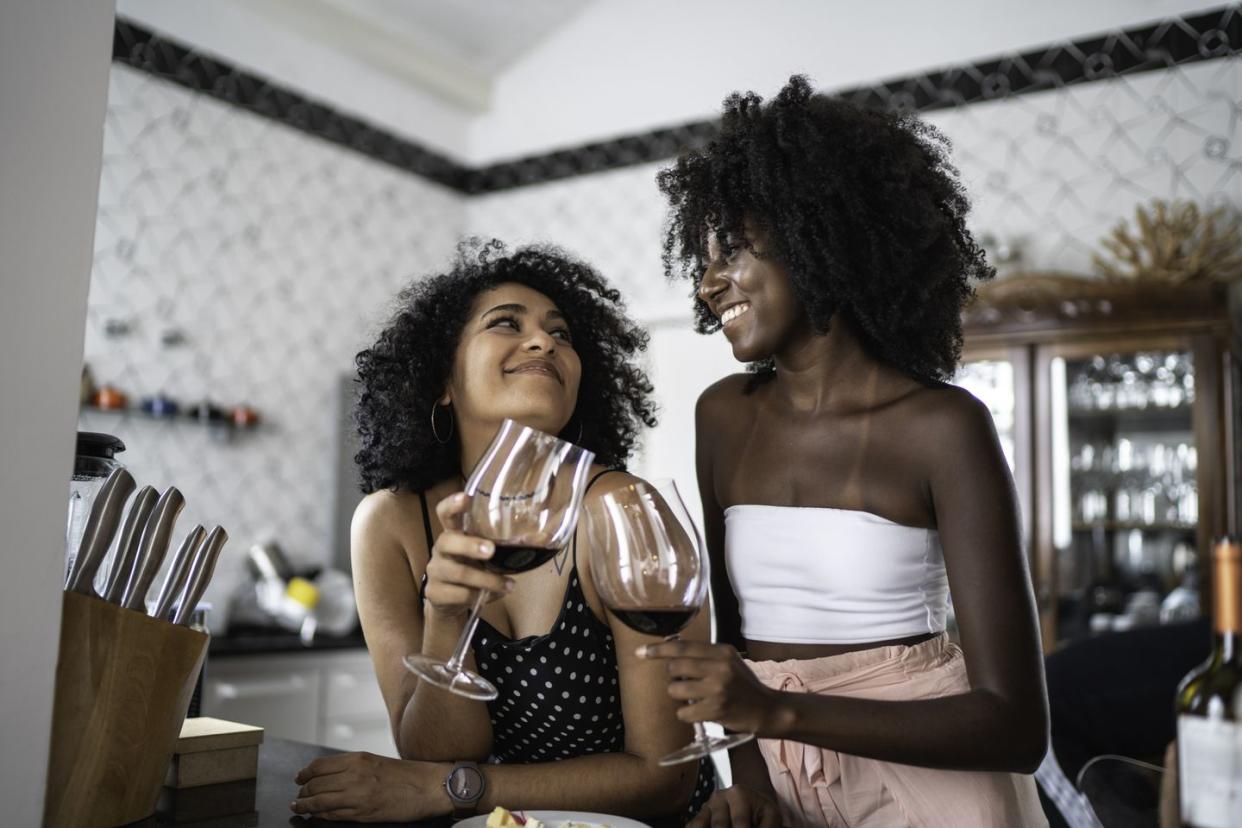 lesbian couple or friends drinking wine at kitchen