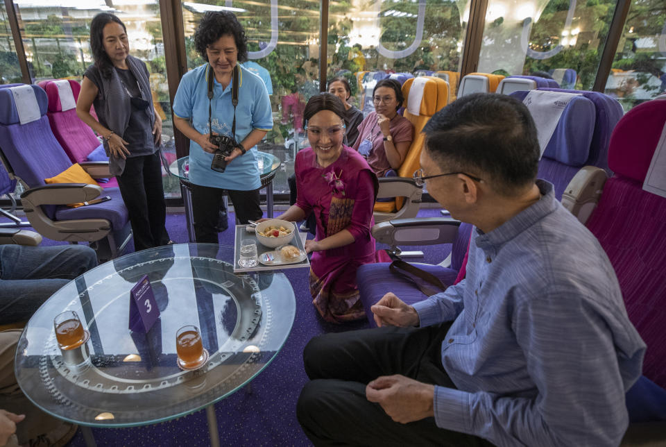 A flight attendant serves meals in a flight-themed restaurant at the Thai Airways head office in Bangkok, Thailand on Oct. 3, 2020. The airline is selling time on its flight simulators to wannabe pilots while its catering division is serving meals in a flight-themed restaurant complete with airline seats and attentive cabin crew. The airline is trying to boost staff morale, polish its image and bring in a few pennies, even as it juggles preparing to resume international flights while devising a business reorganization plan. (AP Photo/Sakchai Lalit)