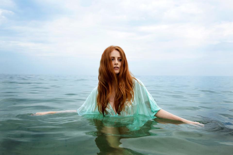 A redheaded model named Alisha from Odessa, Ukraine, swims in water in a green dress