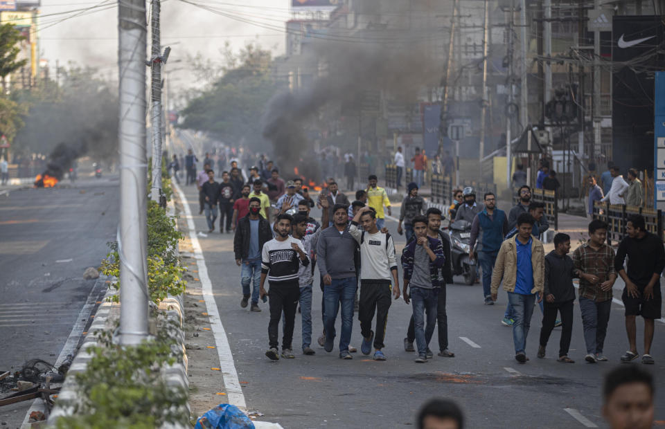 Protestors walk past burning tires defying curfew in Gauhati, India, Thursday, Dec. 12, 2019. Police arrested dozens of people and enforced curfew on Thursday in several districts in India’s northeastern Assam state where thousands protested legislation granting citizenship to non-Muslims who migrated from neighboring countries. (AP Photo/Anupam Nath)