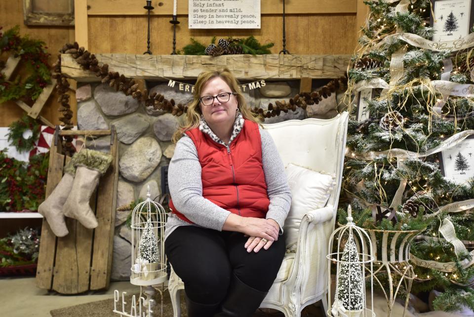 Country Christmas Tree Farm co-owner Theresa Shepherd sits by a decorated fireplace inside the store located at 8122 Bricker Road in Greenwood Township on Monday, Nov. 14, 2022. The farm’s country store sells wreathes, Christmas decorations and craft supplies. In addition to the country store and trees, customers can enjoy wagon rides and hot chocolate.