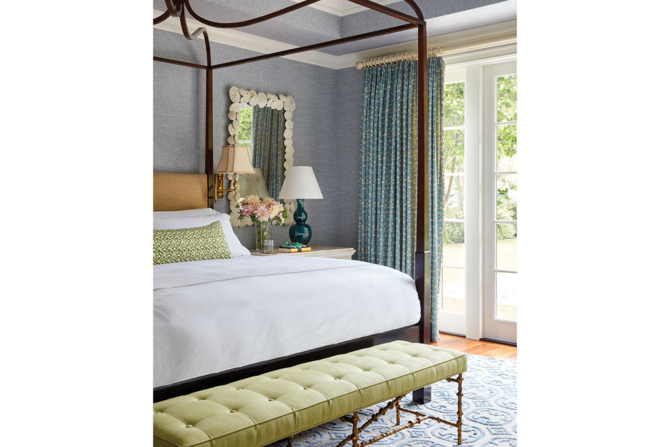 <p>To dial up the serenity in the master bedroom (while still maintaining a visual connection to the rest of the house), Sharpe again looked to the environment to maintain a sense of harmony. “This bedroom opens onto the pool, so there’s this lovely view of blue water and lush greenery that I wanted to reflect inside,” she says. The muted turquoise drapery and navy raffia wallpaper play against one another like varying shades of the ocean, with a faux sea urchin mirror adding another pretty salute to the sea. The mahogany pencil-post bed is by <a href="https://www.rosetarlow.com/" rel="nofollow noopener" target="_blank" data-ylk="slk:Rose Tarlow;elm:context_link;itc:0;sec:content-canvas" class="link ">Rose Tarlow</a>; the bench is by <a href="https://www.olystudio.com/" rel="nofollow noopener" target="_blank" data-ylk="slk:Oly;elm:context_link;itc:0;sec:content-canvas" class="link ">Oly</a>.</p>