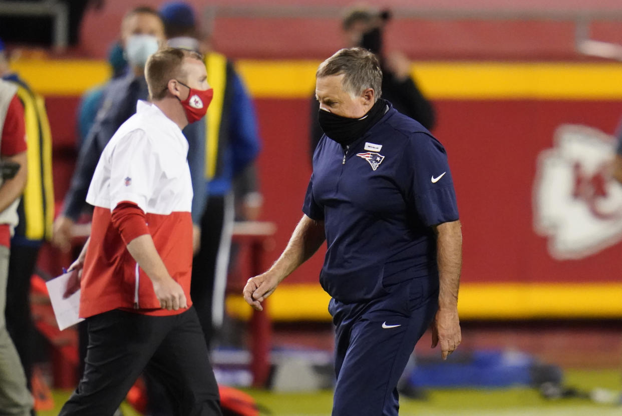 Bill Belichick walks off the field with his head down and masks on.