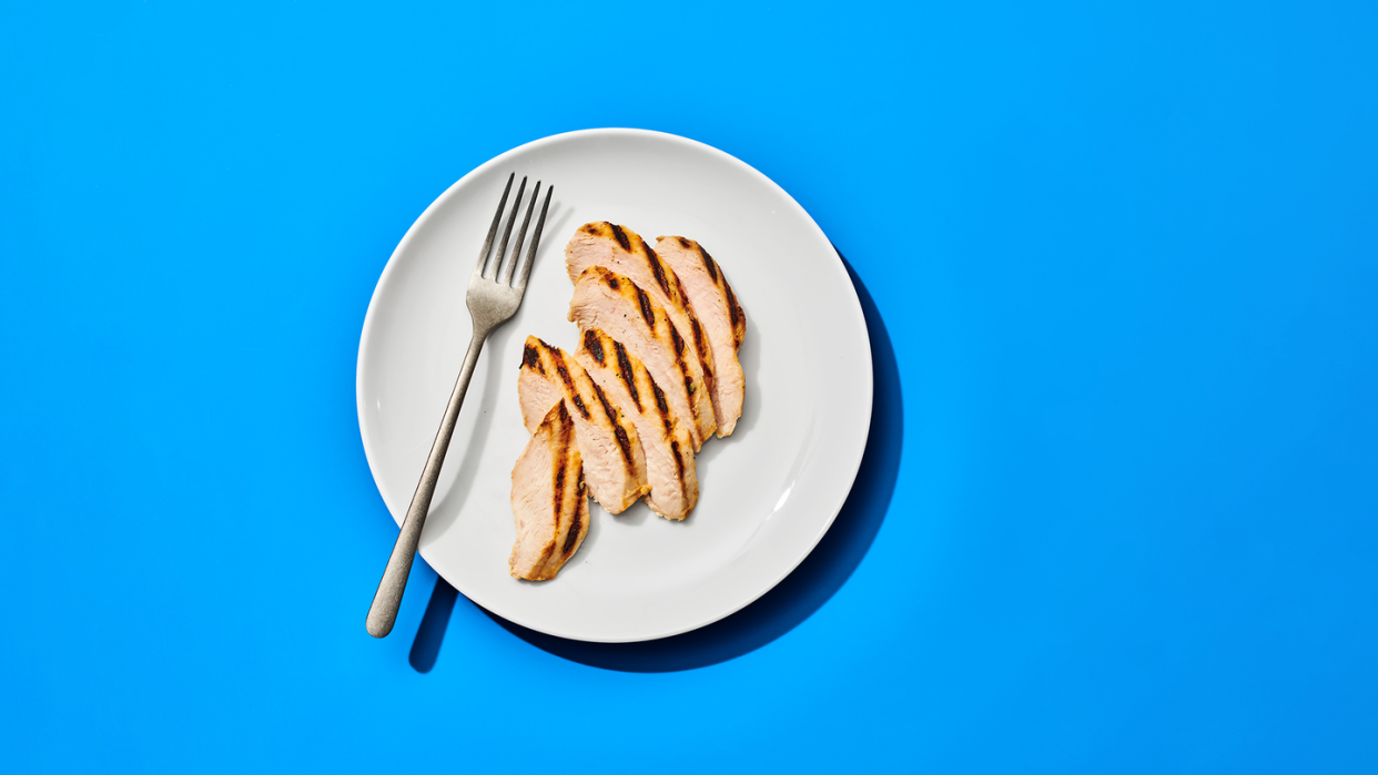 slices of chicken breast on a white plate with a silver fork, on a blue background