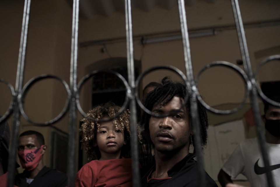 En esta imagen, tomada el 15 de septiembre de 2020, un hombre y un niño miran hacia fuera desde detrás de la verja de hierro de una casa ocupada desde hace casi un año, antes de ser desalojados, en Río de Janeiro, Brasil, en plena pandemia del coronavirus. (AP Foto/Silvia Izquierdo)