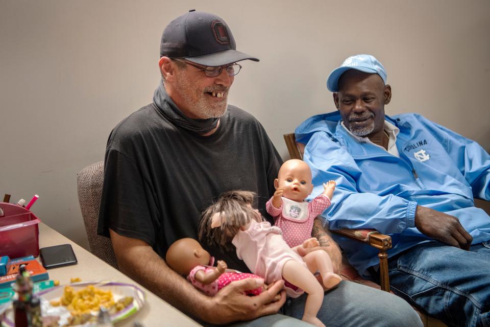 Chris Phillips, left, laughs as he is left with baby dolls by playing children as he sits with Tim Jordan at Trinity Methodist in West Asheville March 31, 2022.