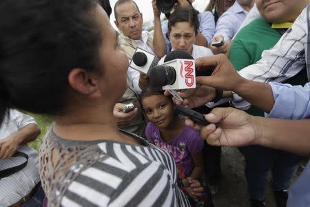 A girl looks at her mother being interviewed by reporters after being deported from the U.S., at the international airport in San Pedro Sula, northern Honduras July 14, 2014. REUTERS/Jorge Cabrera