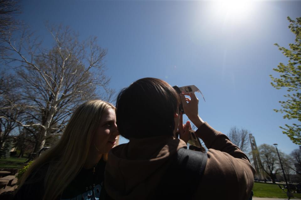 Washburn University students use solar eclipse glasses to take a photo of the sun Monday in front of Memorial Union.