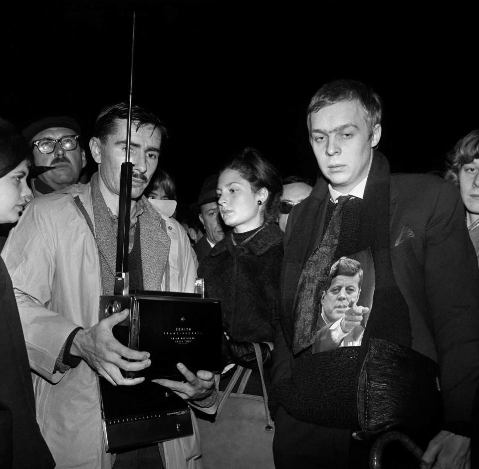 Grave-looking passers-by, including Americans living in France, listen on transistor radios to the latest news about the assassination of US President John Fitzgerald Kennedy, on November 23, 1963 outside the US Embassy in Paris. Kennedy was assassinated on November 22, 1963 in Dallas, Texas, during an electoral tour.