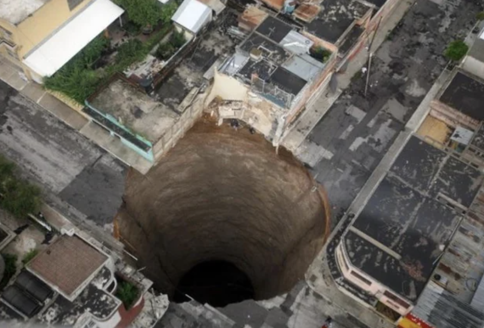 Aerial view of a large sinkhole in an urban street surrounded by buildings