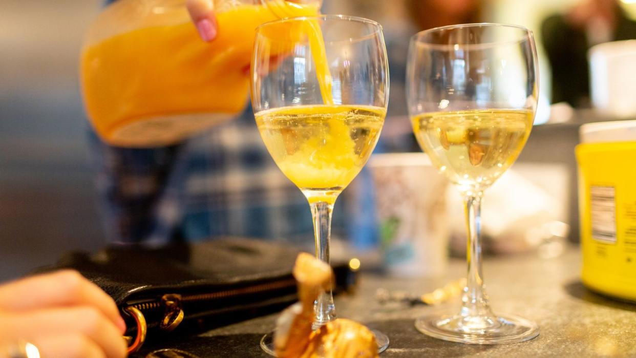 woman pouring orange juice into champagne in glass to make mimosa