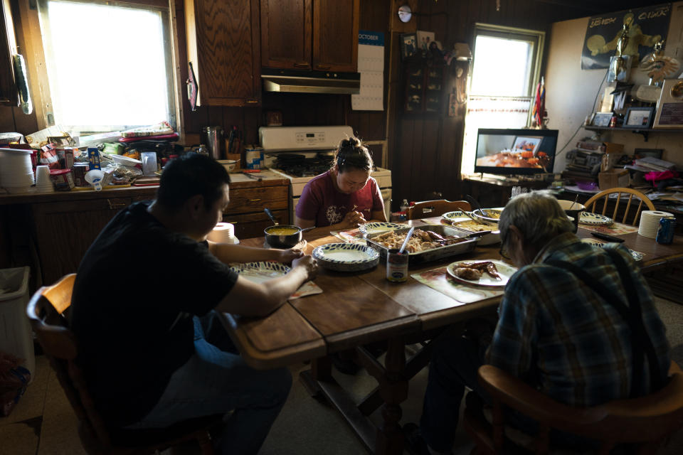 Molly Snell (centro) bendice la mesa al festejar el cumpleaños de su pareja, Tyler Weyouanna (izq), el 1ro de octubre del 2022 en Shishmaref (Alaska). Los acompaña su abuelo Clifford. (AP Photo/Jae C. Hong)