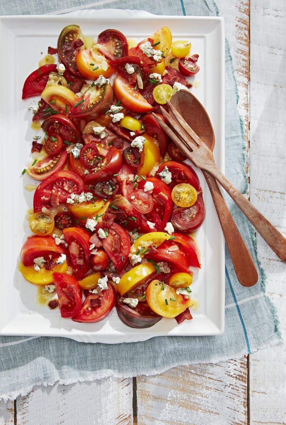 tomato salad with bacon vinaigrette on a white rectangle plate with wooden serving utensils